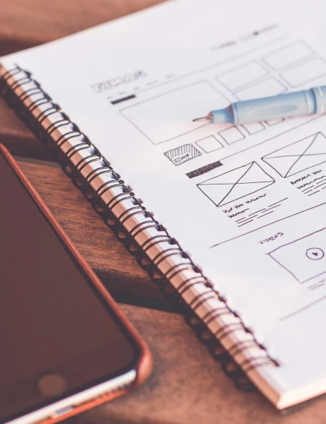 A mobile phone sitting next to a notebook with a wireframe sketch