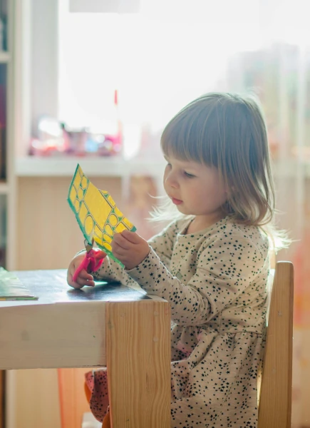 A little girl sitting down cutting paper